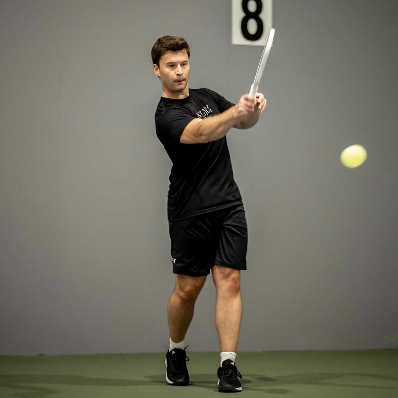 will ventura hitting a pickleball serve wearing a black FLIK athletic shirt and black shorts
