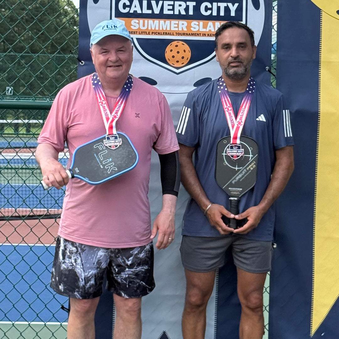  two pickleball players on the winners podium.  One is holding a FLiK F1 pickleball paddle and wearing FLiK branded athletic shirt