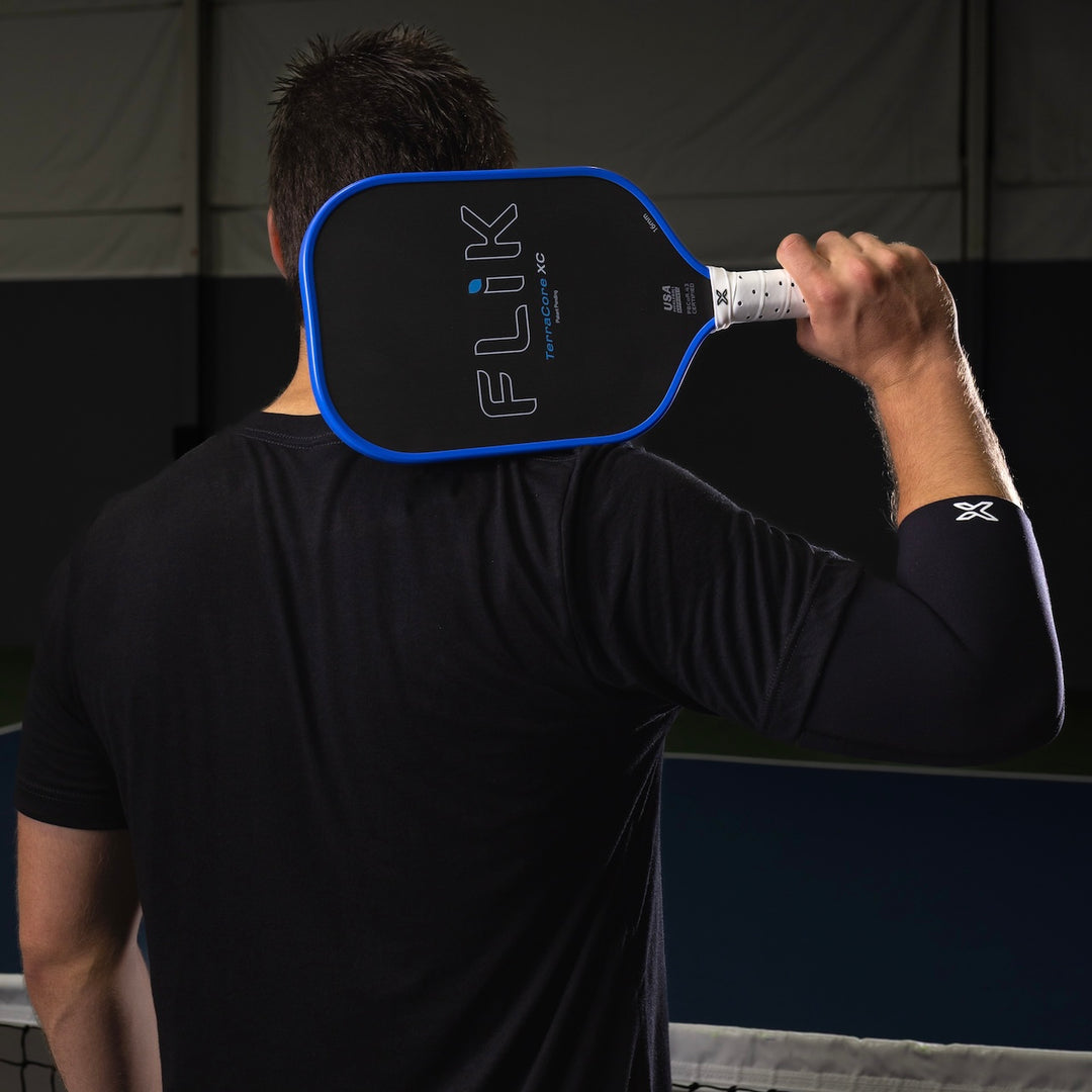 Person holding a pickleball paddle with 'Flik' branding against a dark background
