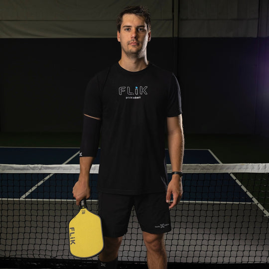 Man holding a yellow pickleball paddle with 'FLIK' branding on a tennis court.
