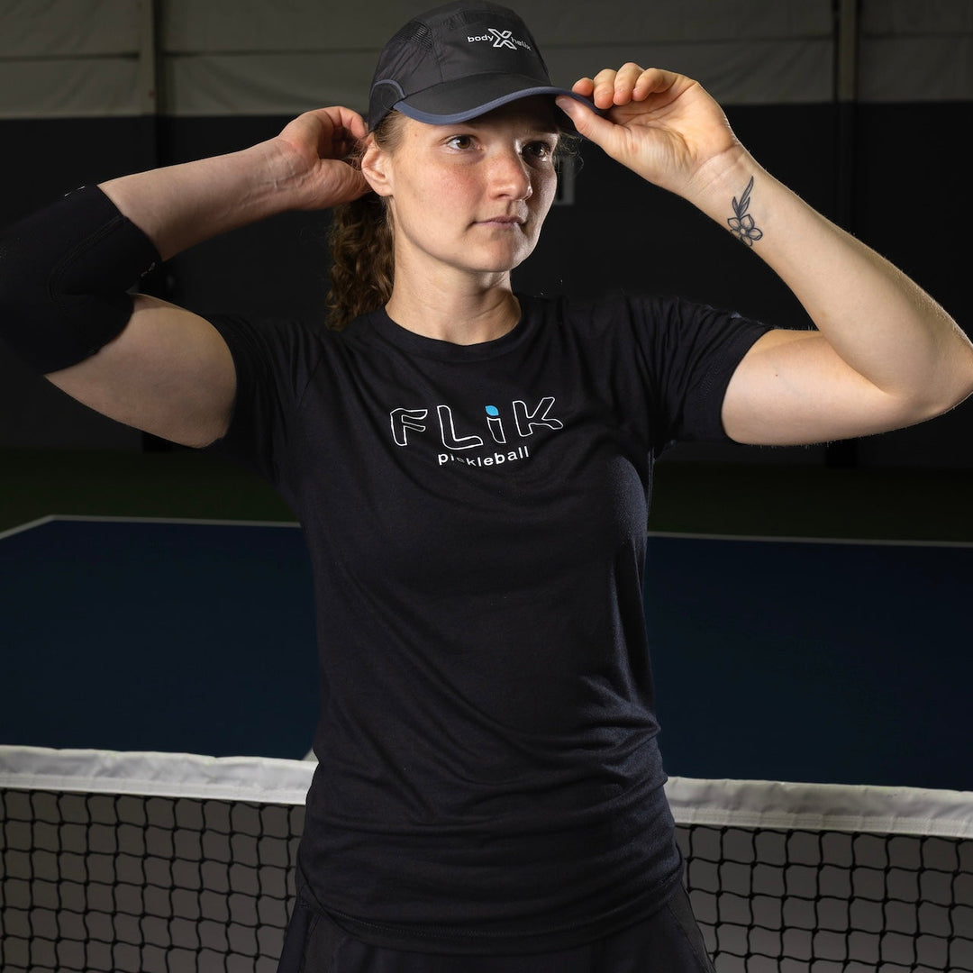 Person wearing a black cap and black t-shirt with 'FLIK' logo on a sports court.