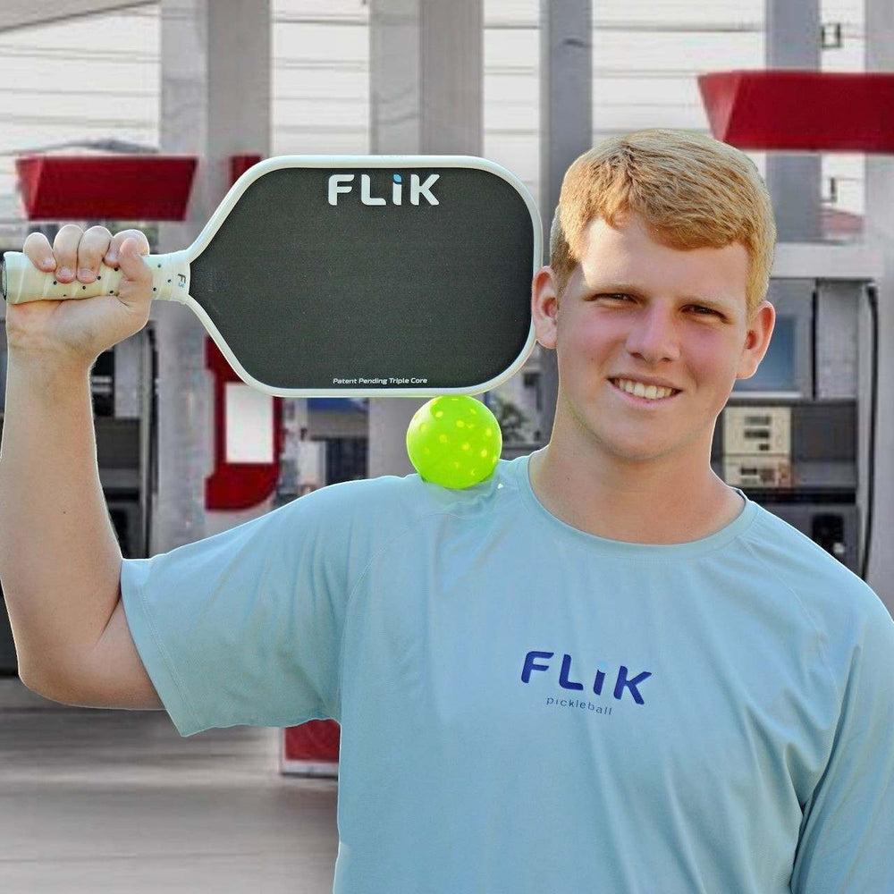 A man standing at a gas station with a FLik F3 Triple Core pickleball paddle and a ball on his shoulder