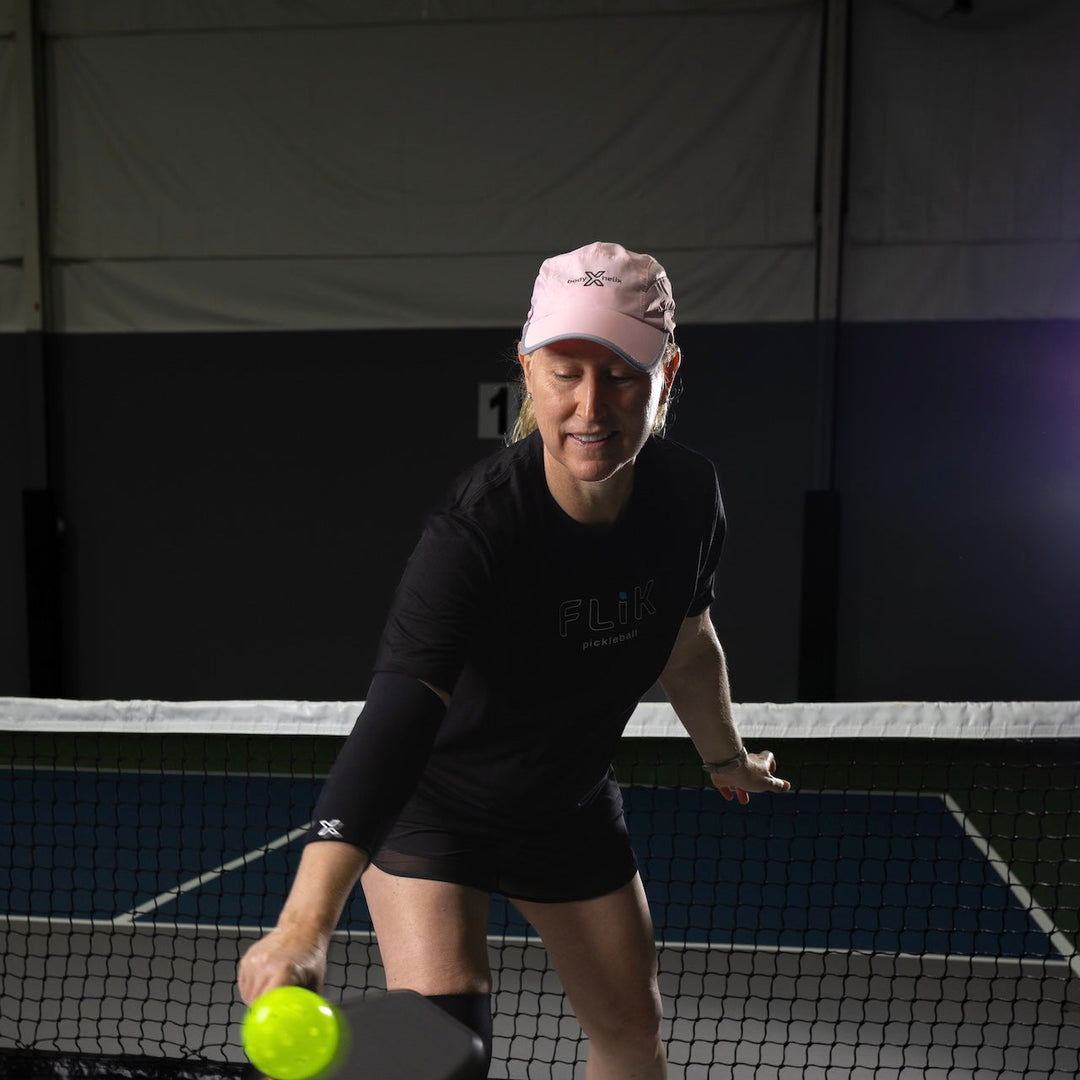 Woman playing paddle ball on an indoor court wearing a black shirt and pink cap.