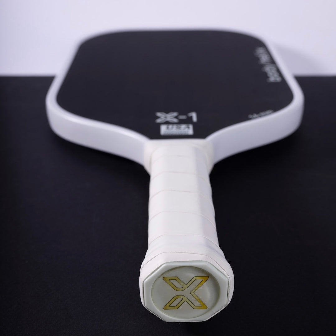 White and black pickleball paddle with 'X' branding on a black surface