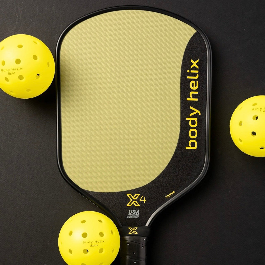 Body Helix pickleball paddle with three yellow pickleballs on a black background