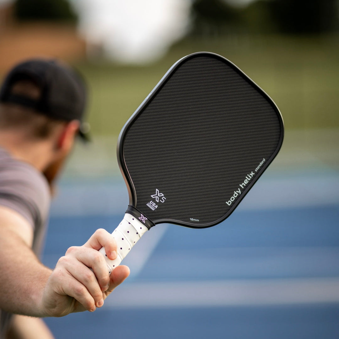 Person holding an X5 pickleball paddle with 'body helix' branding on a blurred pickleball court