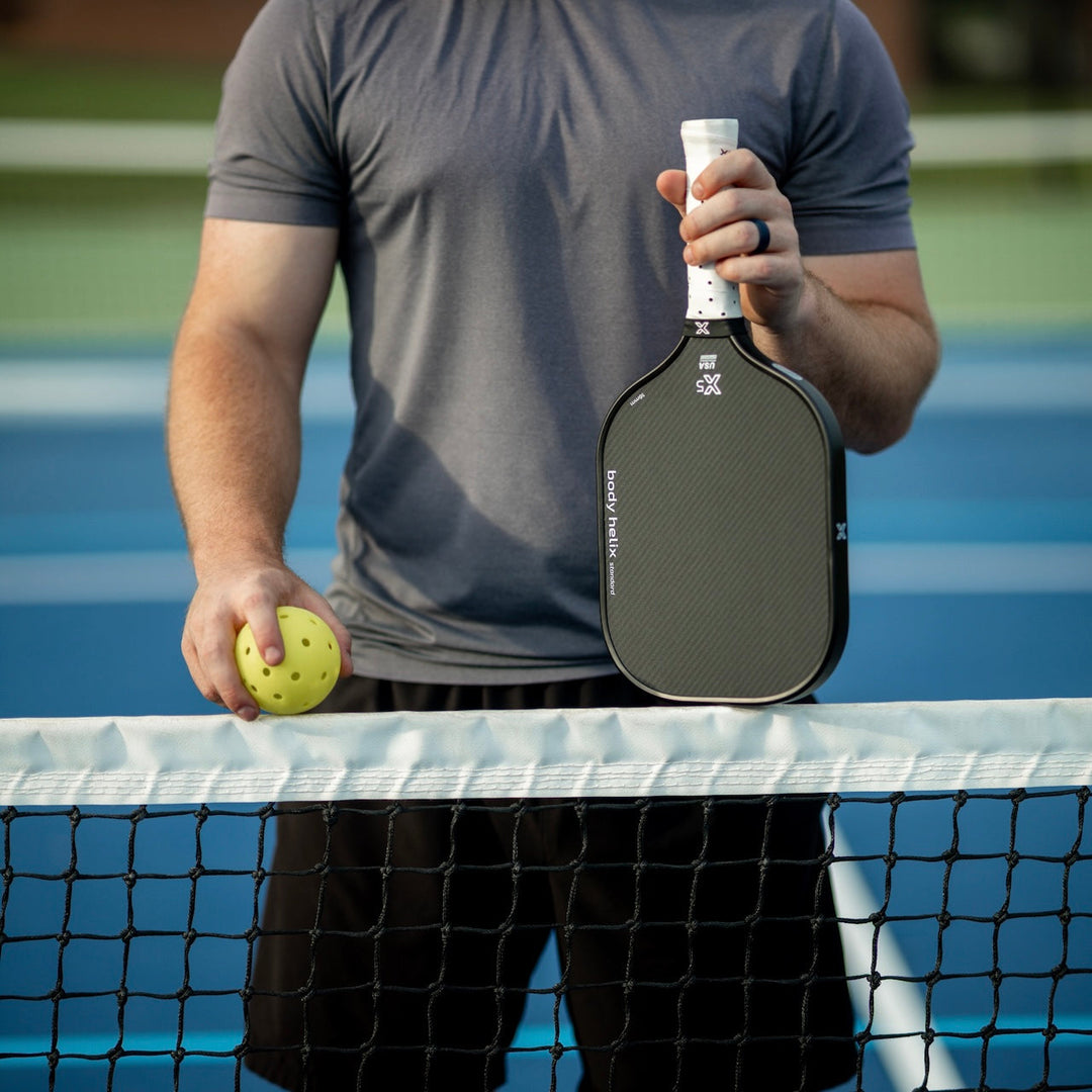 Person holding an body helix X5 pickleball paddle and ball on at a pickleball net
